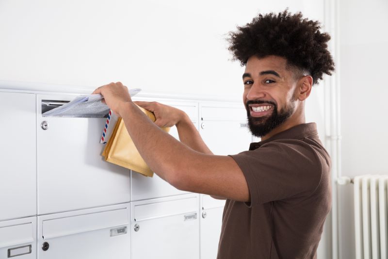 Un jeune postier dépose un avis de passage dans une boîte aux lettres