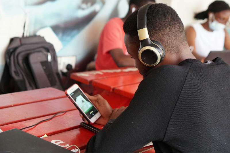 jeune homme noir de dos en train d'écouter de la musique sur Spotify avec son smartphone et un casque audio