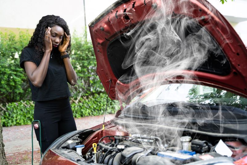 Femme qui regarde choquée, la fumée qui sort du moteur de sa voiture