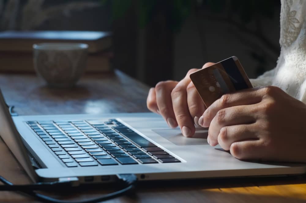 homme, avec une carte bancaire à la main, résiliant son crédit Carrefour Banque depuis son ordinateur