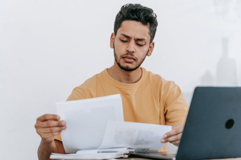 jeune homme, avec des documents à la main, résiliant son contrat Mutuelle du Nickel sur un ordinateur portable