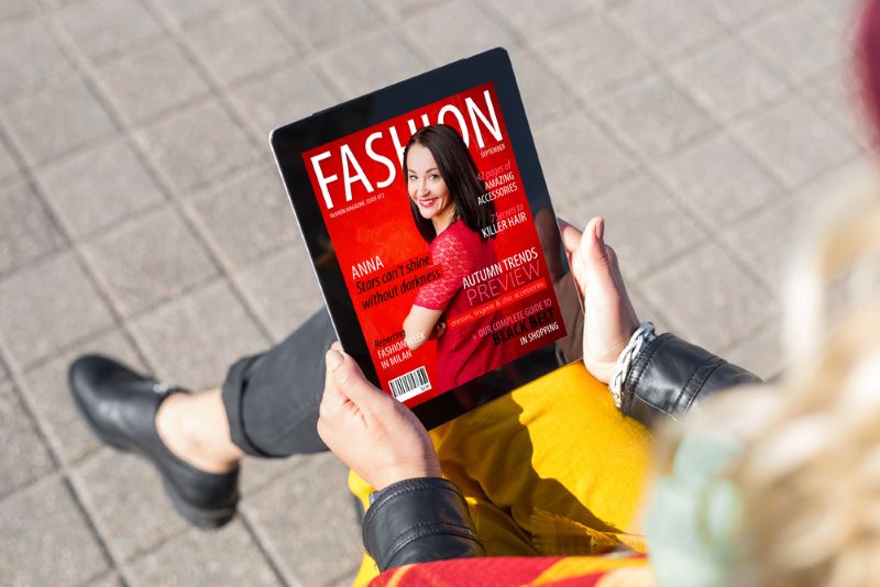 Une jeune femme assise lit la rubrique Mode de son magazine en ligne Cosmopolitan