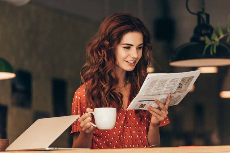 Une jeune femme tient une tasse de café à la main et lit son journal Le Bien Public