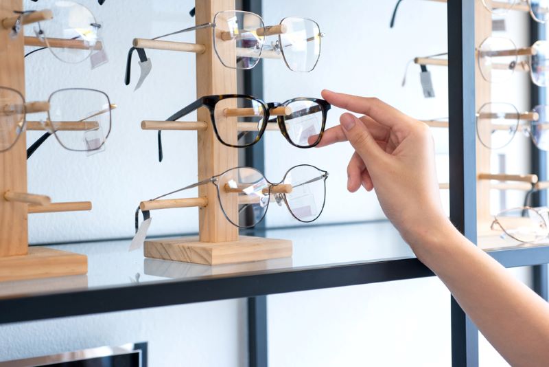 Une main de femme choisit une paire de lunettes sur le présentoir de l'opticien.