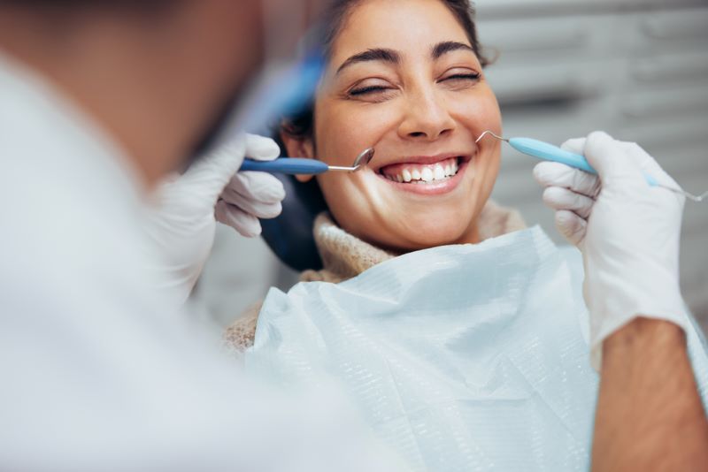 Une jeune femme sourit à son dentiste qui s'apprête à contrôler l'absence de caries dans sa bouche