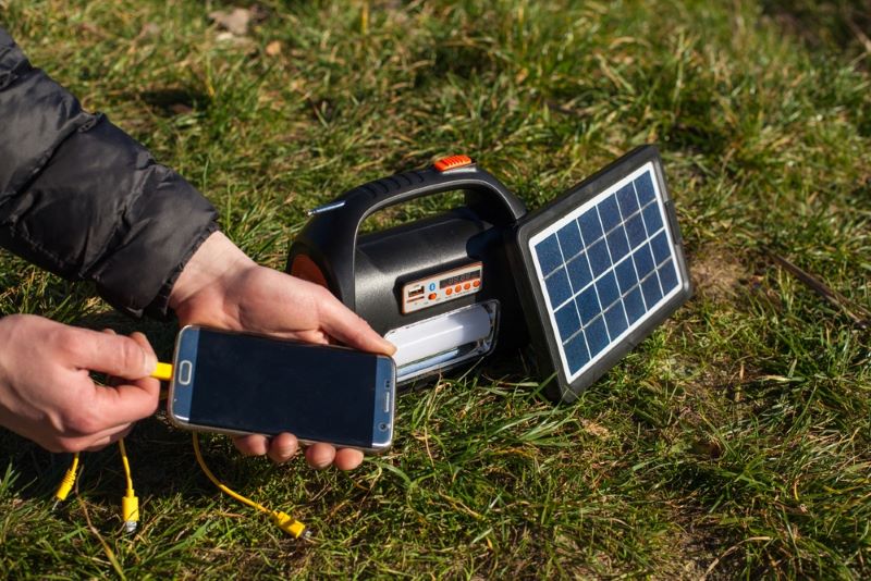 Une main d'homme fait un branchement avec un téléphone mobile et un petit panneau solaire pour avoir une connexion internet 