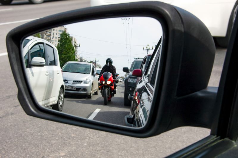 Le conducteur regarde dans son rétroviseur la moto qui remonte la file de voitures
