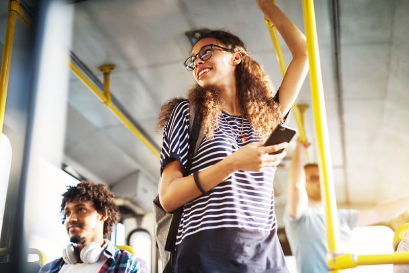 Jeune fille dans un bus qui sourit et tient son portable à la main
