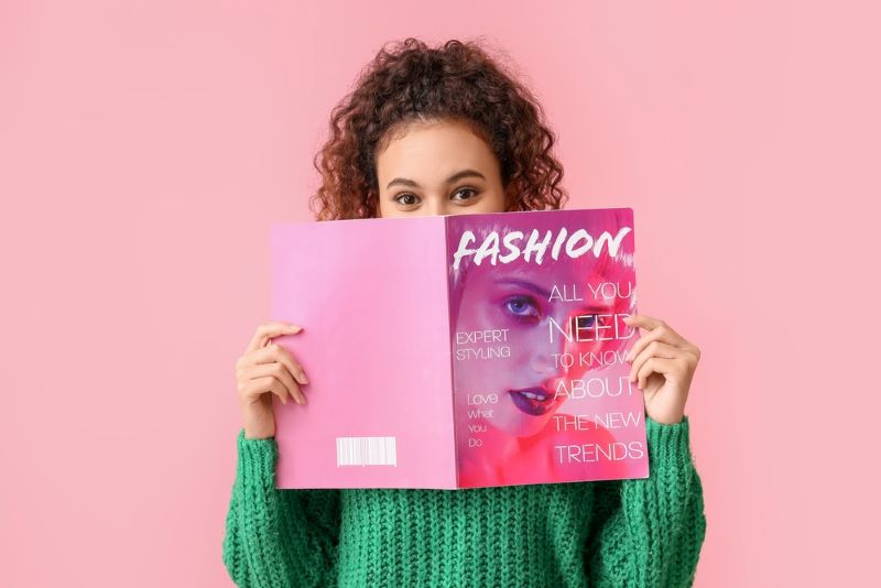 Jeune femme cachée derrière le magazine de mode qu'elle est en train de lire