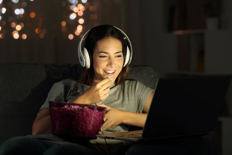Adolescente qui regarde un film Netflix sur son ordinateur portable en mangeant un snacking