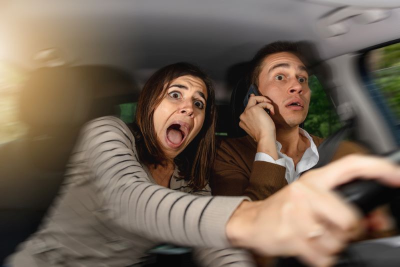 Couple en voiture : le monsieur téléphone et la femme essaie d'éviter un accident