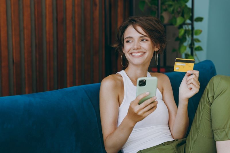 Une jeune femme tient en main une carte bancaire Matmut et son portable pour faire des achats en ligne