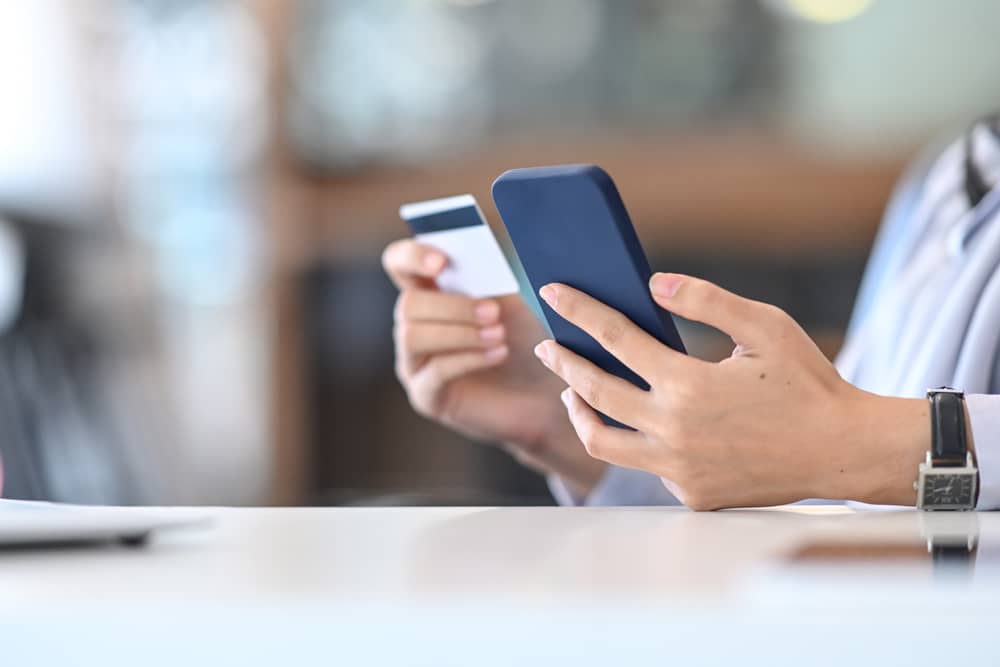 mains d'une personne tenant sa carte de crédit CIC et son smartphone