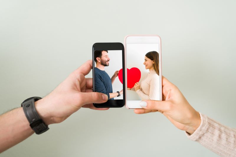 Les mains d'un couple rapprochent leurs portables avec, en image de fond, leur photo tenant les deux parties d'un coeur réuni