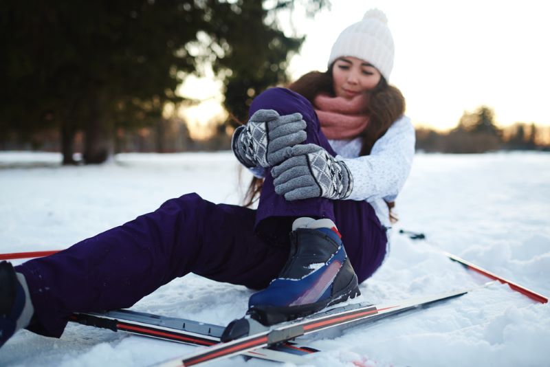Une femme est tombée en ski et se tient la jambe.