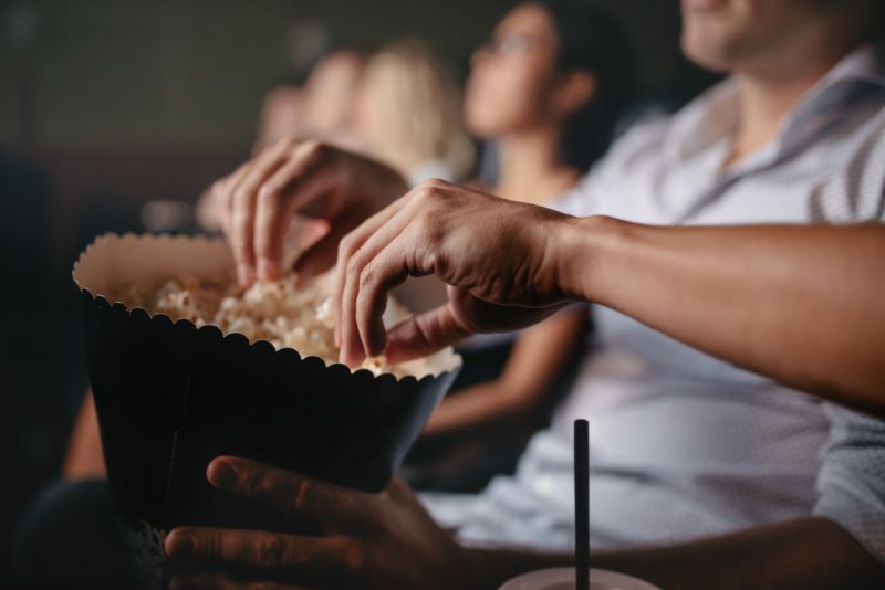 Des mains de spectateurs plongent dans un sac de popcorn pendant une séance de cinéma