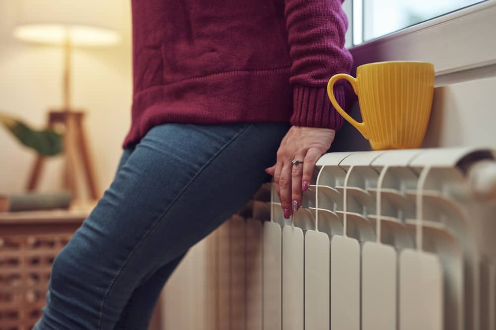 femme appuyée contre un radiateur alimenté par Primeo Energie